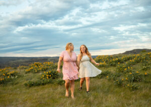 Mom and daughter holding hands in wildflower field during sunset in Oregon.