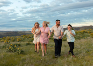 Family of four laughing and running in a field in Oregon. 
