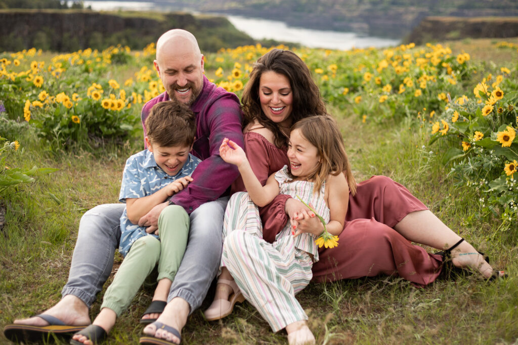 Family of four laughing while sitting in yellow wildflowers near Hood River, Oregon. Hood River Waterfront Park.