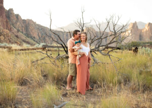 Family of three with infant standing in front of fallen tree at Smith Rock State Park, Oregon. 