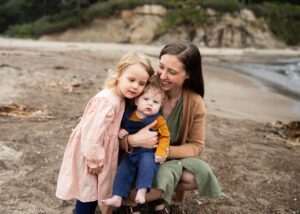 Mother with two young children snuggles on the Oregon Coast shoreline. Photo featured in a blog about how much does family photography cost?