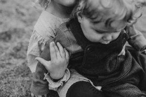 Oregon Coast photographer takes a black and white image of a young sibling's hand on her brother. 