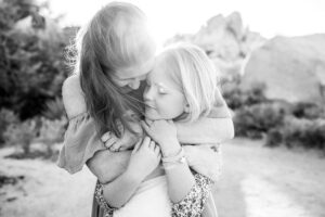 Mom and daughter hug against the rugged terrain in Joshua Tree for family photos.
