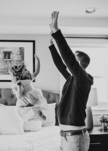 Black and white image of daughter high fiving her dad during a newborn photo shoot. Newborn Photo Ideas. 