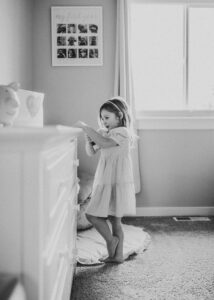 Black and white image of a little girl in her room wearing a mid-length dress for what to wear for newborn photos blog. 