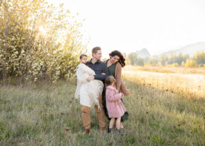 Family of four laughing and hugging in a field for winter family photos. 