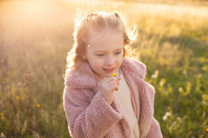 Little girl in pink jacket holding a flower at sunset in a field. 