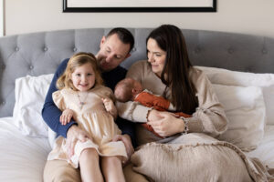 Photo of family sitting on bed with newborn, DIY newborn photo ideas. 
