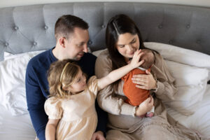 Family of four on bed with young girl and newborn baby boy. 