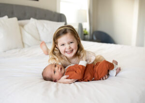 DIY newborn photos. Little girl holding her baby brother on a bed. 
