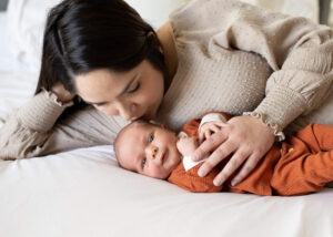 Mother kissing her newborn baby on the head while laying on the bed. Newborn photo ideas. 