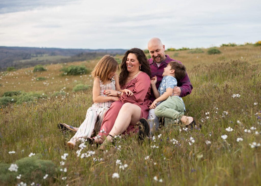 The family is sitting in wildflowers at Rowena Crest for family photos.