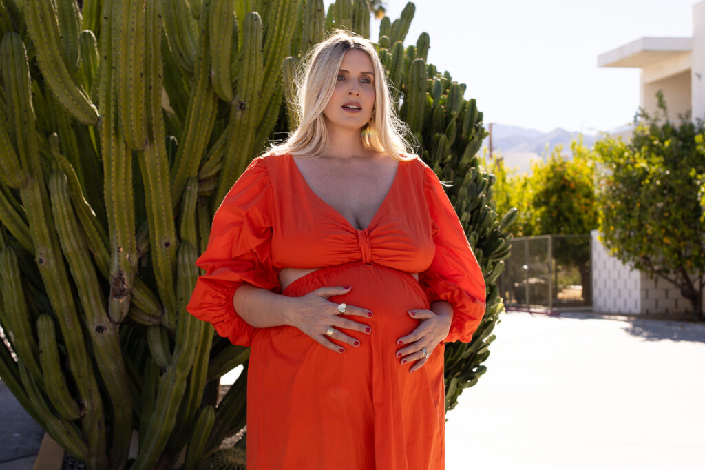 Blonde pregnant woman standing in front of cactus at the Ace Hotel. 