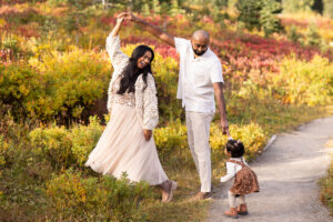 Parents dance in fall foliage while laughing with young daughter for Mt Rainier family photos