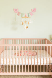 Newborn photos featuring a swaddled baby sleeping in a blush crib inside a light-filled nursery, and is featured in an article about What Newborn Photos Look Like at 2–6 Weeks Old