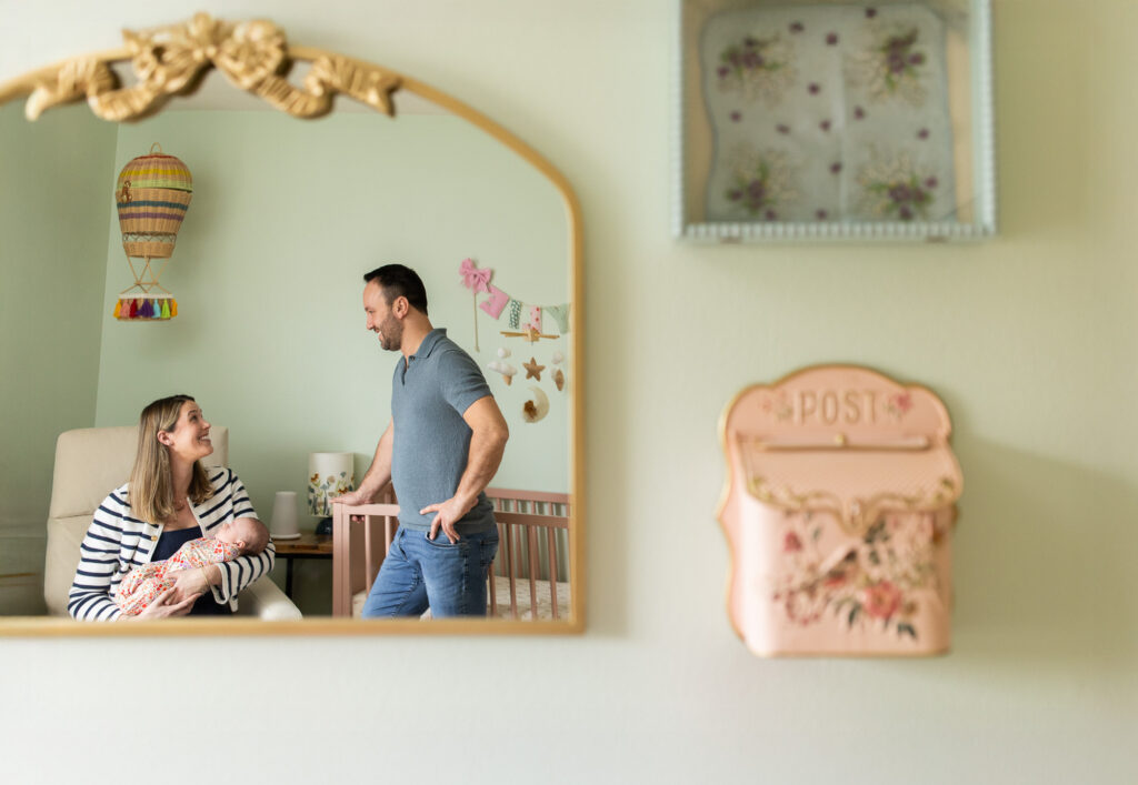 Parents with newborn in nursery during a bump to baby experience, mother holding baby while talking with partner in a relaxed in-home photography session