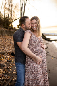 Pregnant couple embracing during a bump to baby experience maternity session at sunset, with hands gently resting on baby bump outdoors. 
