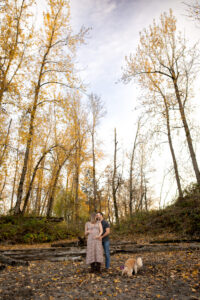 Couple standing together during a bump to baby experience maternity session surrounded by fall trees and natural landscape. 