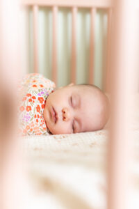 Sleeping newborn baby in crib during a bump to baby experience in-home session, wrapped in floral swaddle with soft natural light