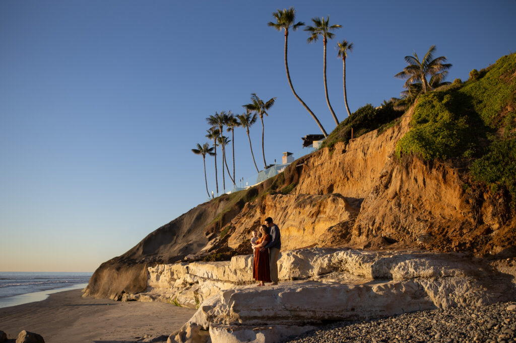 Young family holds their toddler at a sunset beach family photo shoot. 