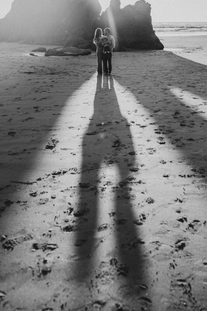 Black and white photo of a family with a baby standing on the beach at sunset.