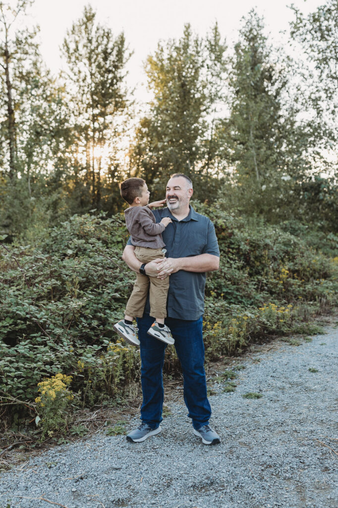 Father and son share a moment of laughter during family photos at sunset. 