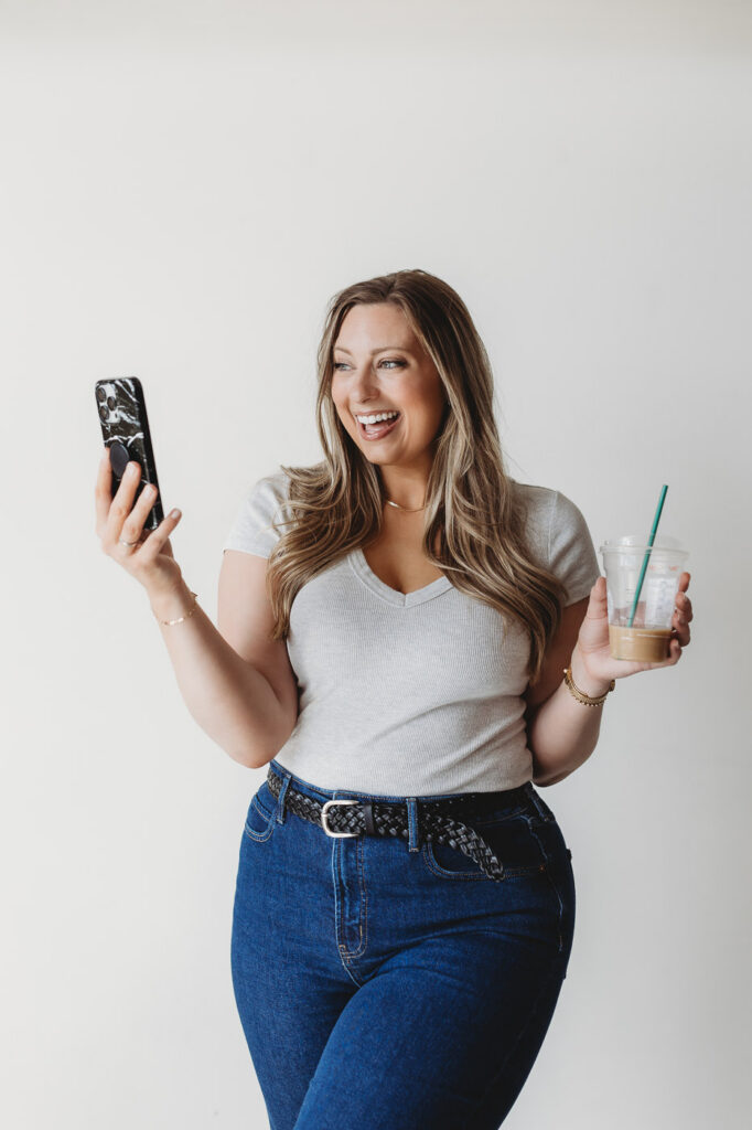 women smiles at her phone as she hold an iced coffee during a headshot session for her business. Featured in a blog about, are branding photos worith it for a small business?